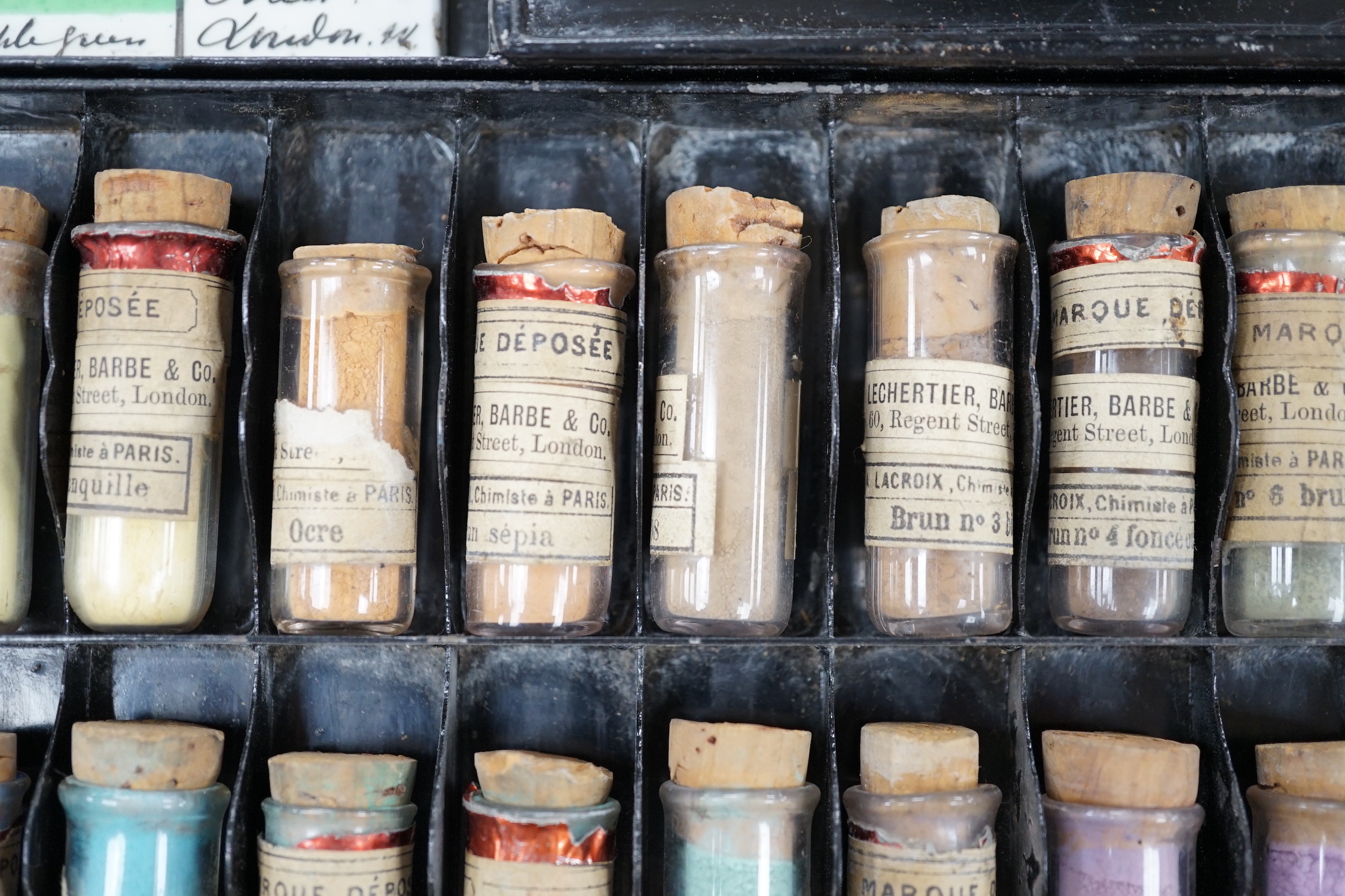 A black artist's tin box, with fitted interior, containing glass phialls of coloured shades of powdered paint and a white glass samples panel etc, box 37.5cm wide, 27cm deep